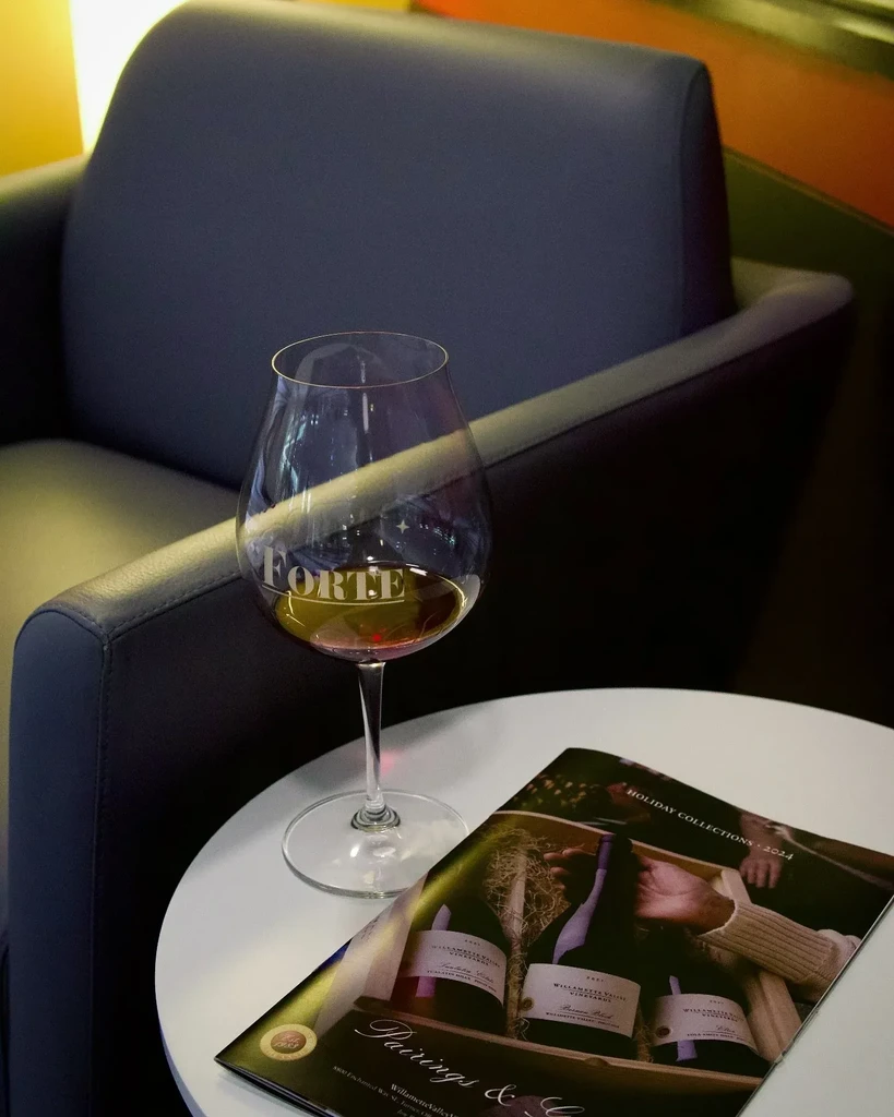 Dimly lit scene: FORTE red wine glass and Holiday Collections magazine.