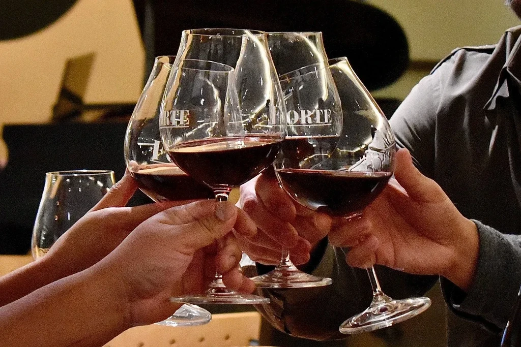 Four hands toast with red wine in glasses labeled "FORTE".