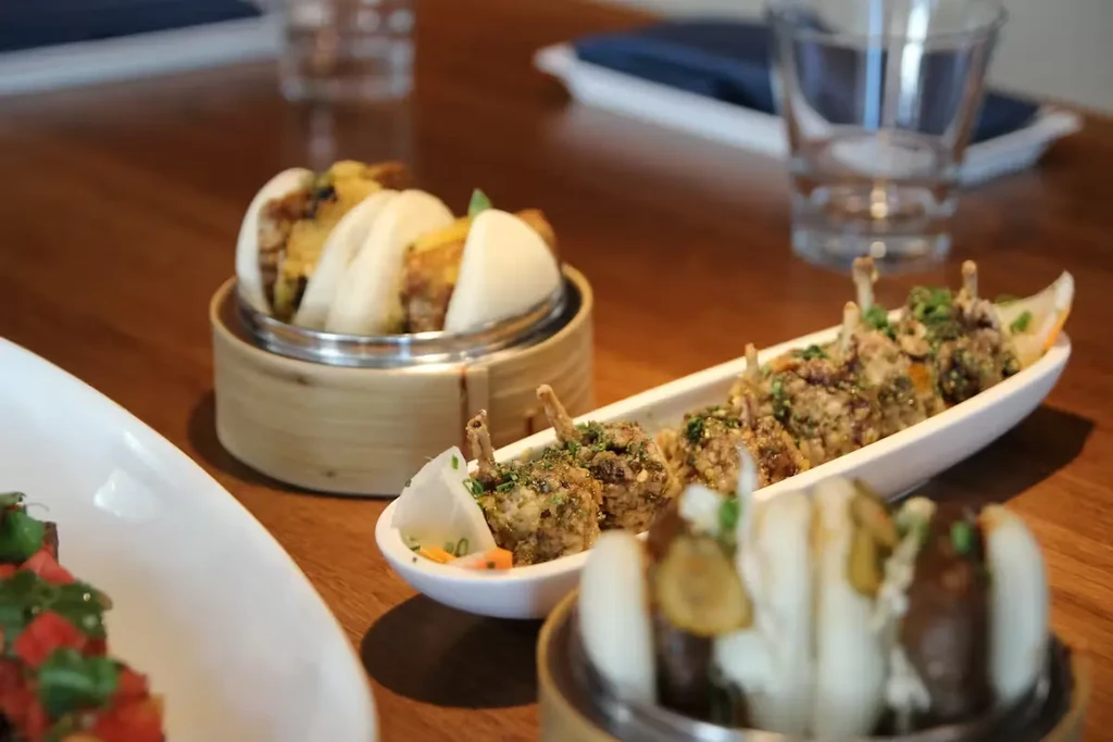 Bao buns, fried morsels, and colorful salad on a wooden table.