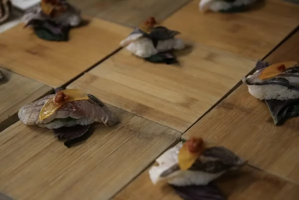 Nigiri sushi with fish, roe, and leaf garnish on wooden planks.