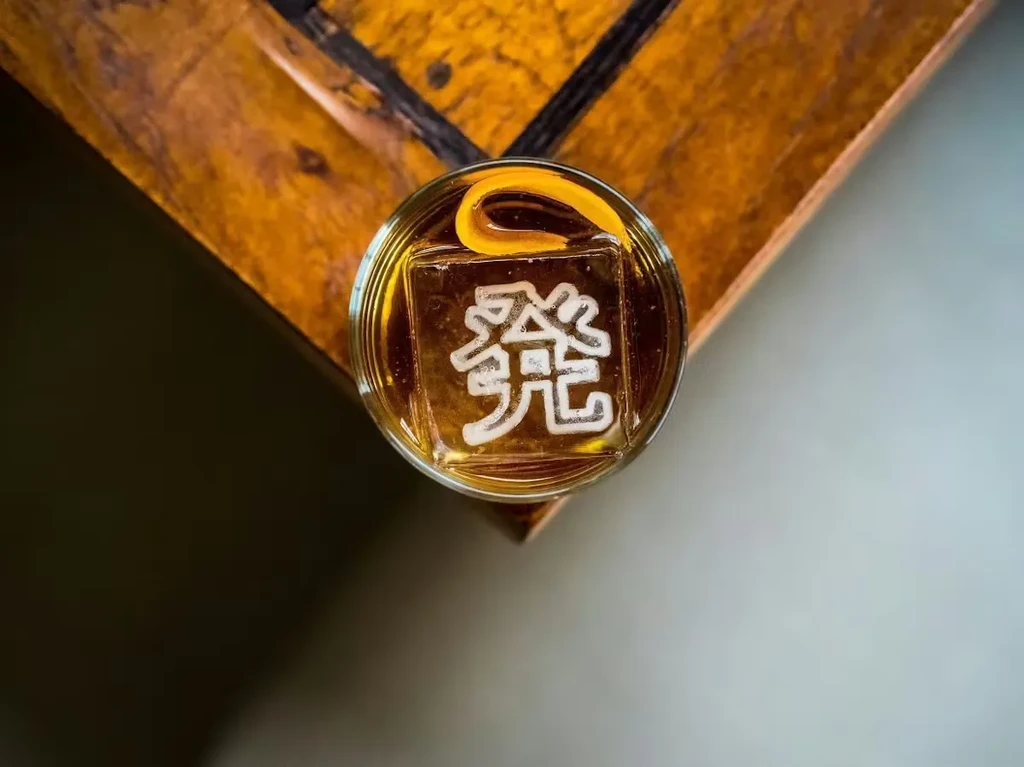 Amber cocktail with embossed '發' ice and orange peel.