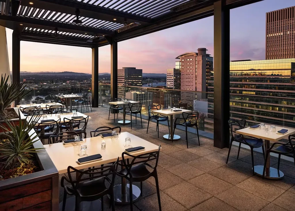 Empty modern rooftop dining terrace overlooking a city at dusk.