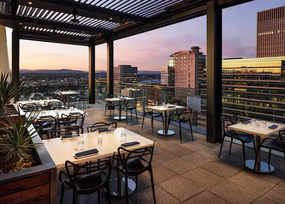 Empty modern rooftop restaurant patio with city view at sunset.