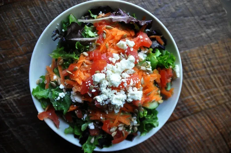 Salad with lettuce, carrots, tomatoes, feta, and sunflower seeds on wood.