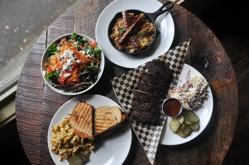 Four varied dishes: salad, grain, seasoned meats, and grilled sandwich.