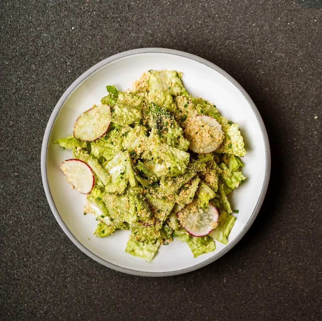 Green salad with radishes, herbs, and toasted topping on white plate.