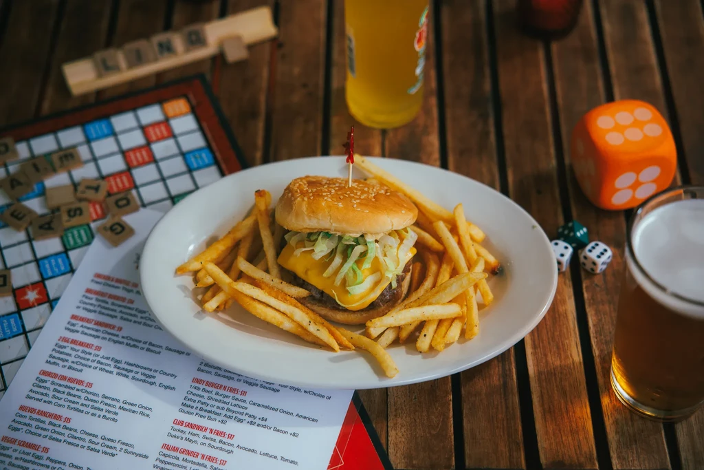 Overhead shot of cheeseburger, fries, beer, dice, and Scrabble game.