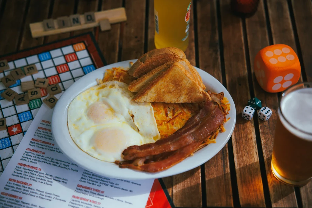Hearty breakfast with fried eggs, bacon, hash browns, toast, and games.