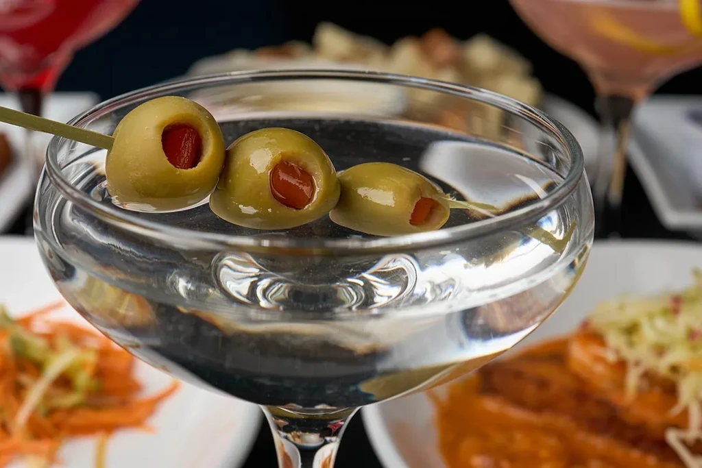 Martini glass with clear liquid and pimento-stuffed olives on a pick.