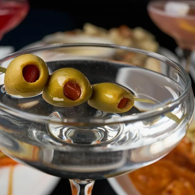 Close-up of a clear cocktail with three skewered green pimento olives.