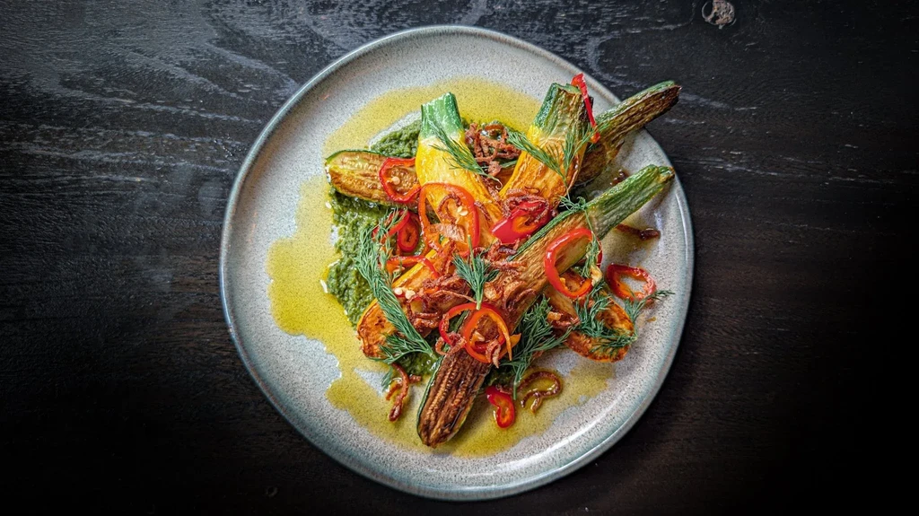 Grilled zucchini and squash dish with green sauce and garnishes.