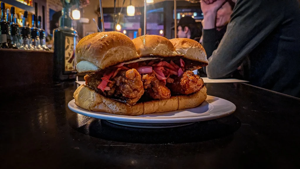 Large fried chicken sandwich with pickled onions at a dim bar.