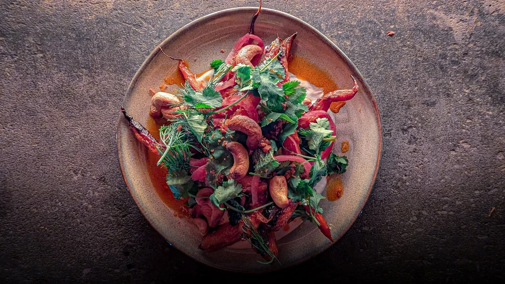 Overhead: Roasted carrots, cashews, herbs, and sauces on an earthy plate.