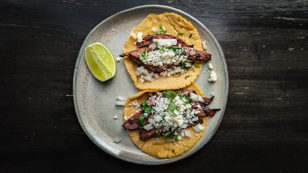 Two grilled steak tacos with cheese, onions, cilantro, and lime.
