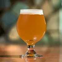 Hazy amber beer with white foam in a glass on a table.