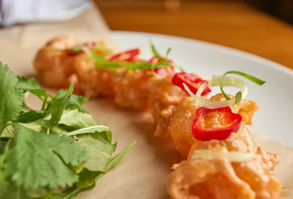 Close-up of fried seafood with orange sauce, chili, green onion, and salad.