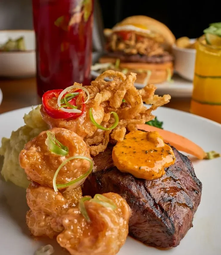 Seared steak with orange sauce, fried shrimp, mashed potatoes, and crispy onions.