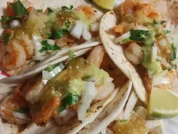 Three shrimp tacos with onions, cilantro, salsa verde, and lime.