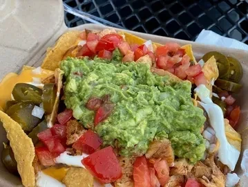 Nachos topped with guacamole, cheese, meat, and vegetables in a container.