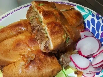 Shredded meat stuffed bread, radishes, and lime on a colorful plate.