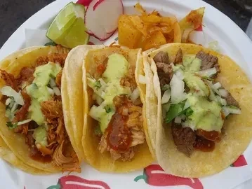 Three vibrant tacos with varied fillings, cilantro, onion, and green sauce.