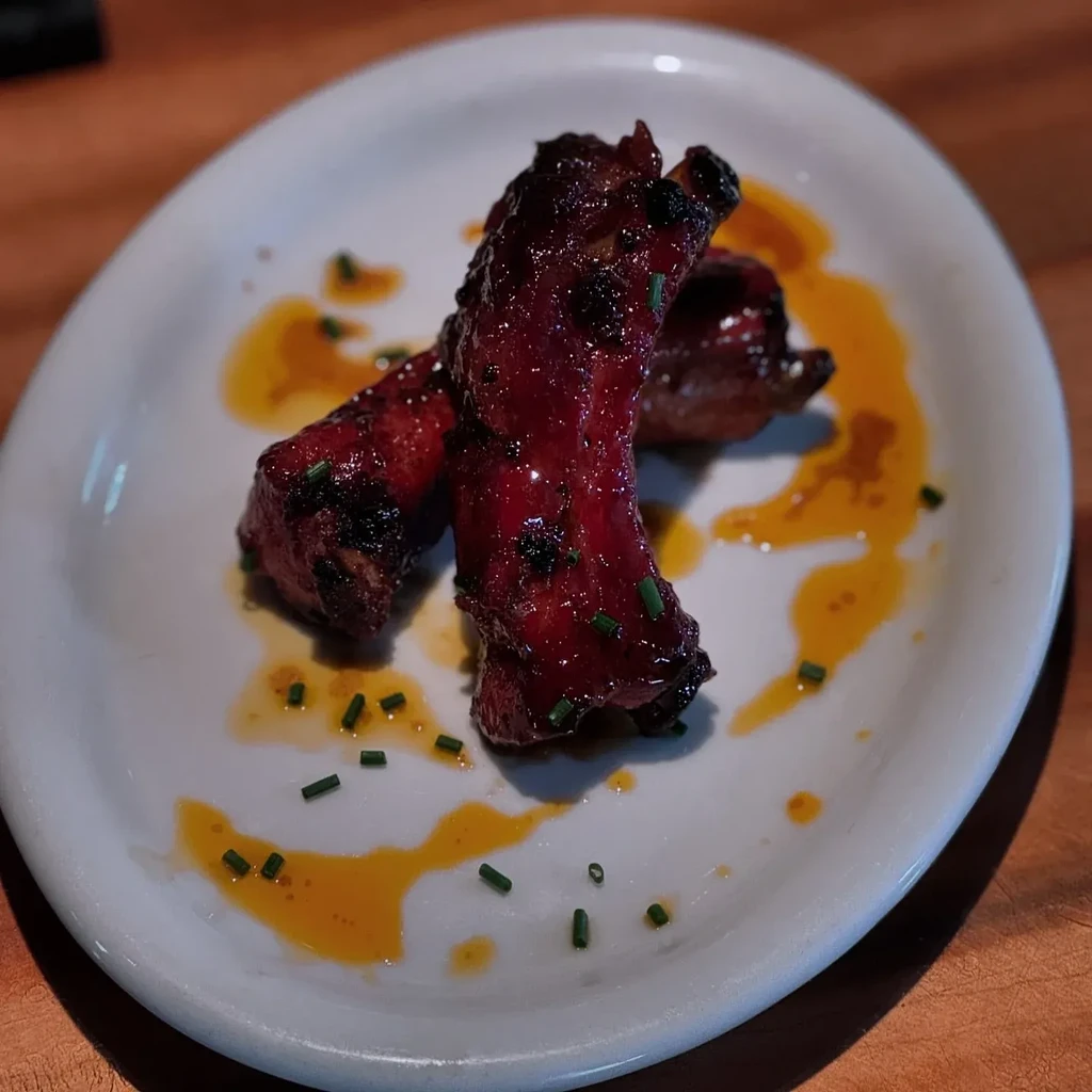 Two glazed barbecued spareribs on a white plate with sauce and chives.