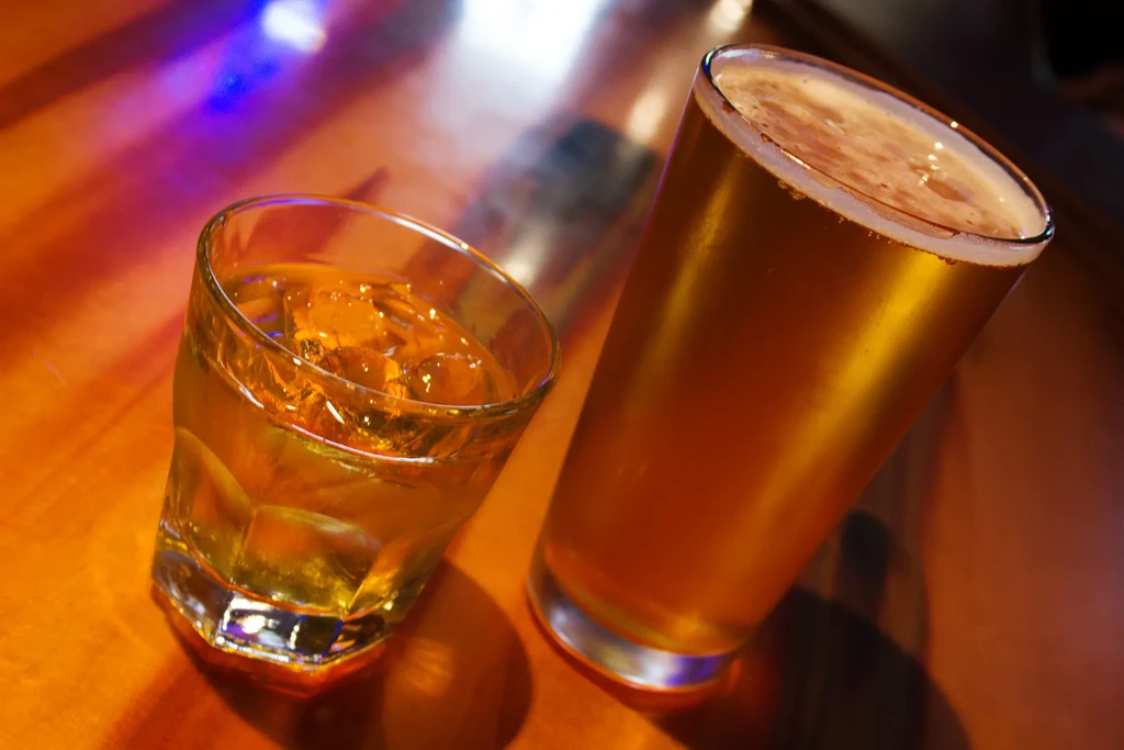 Whiskey on rocks and a pint of beer on a wooden bar.