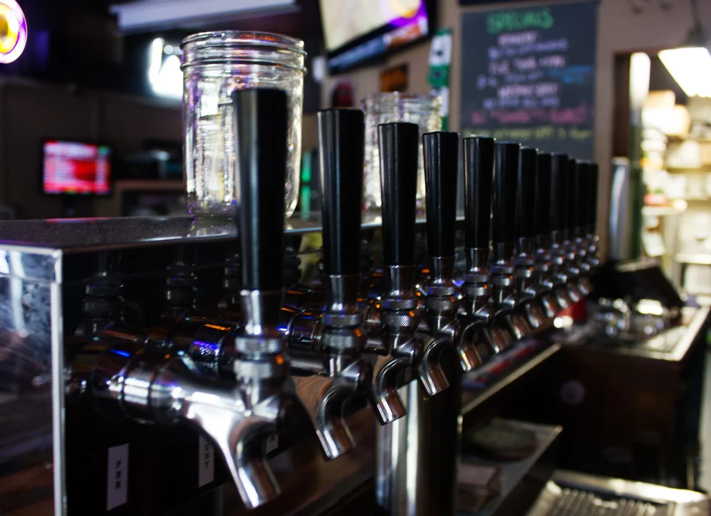 Close-up of beer taps and a mason jar in a blurred bar.