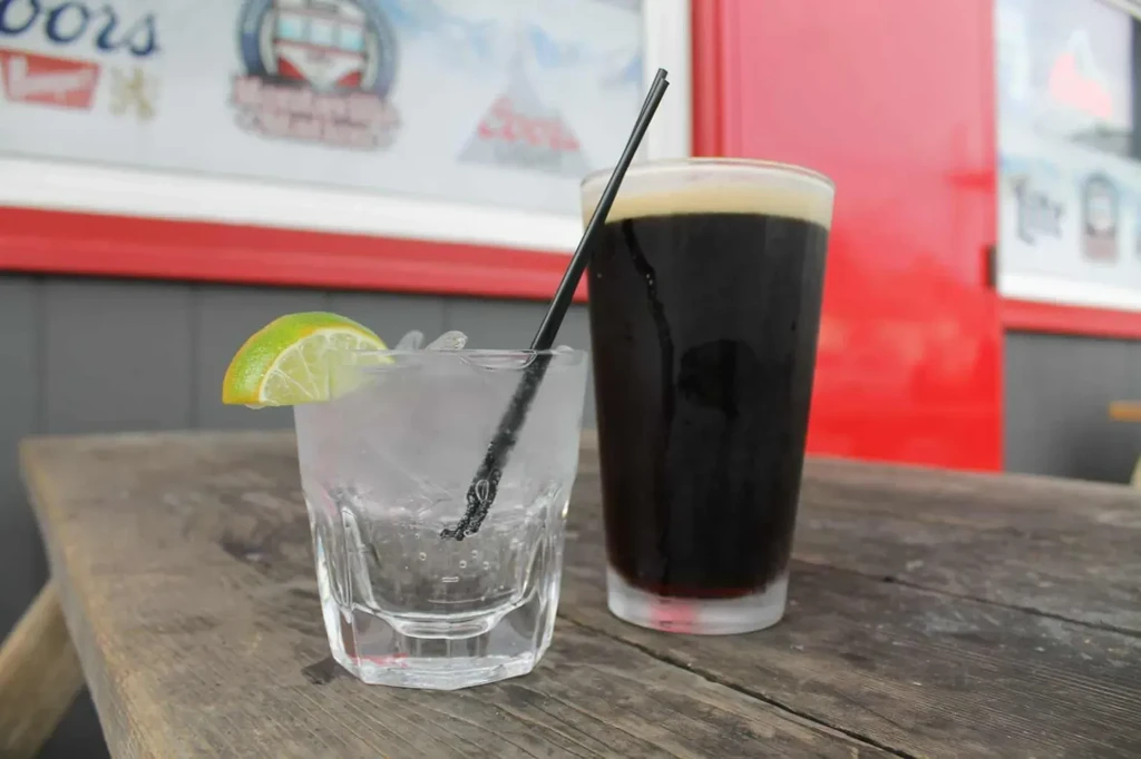 Two drinks: clear with lime, dark with foam, on a rustic table.