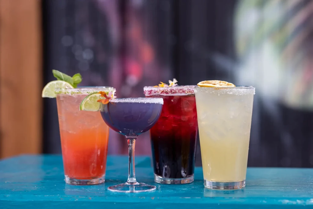 Row of four colorful cocktails with unique garnishes and decorative rims.