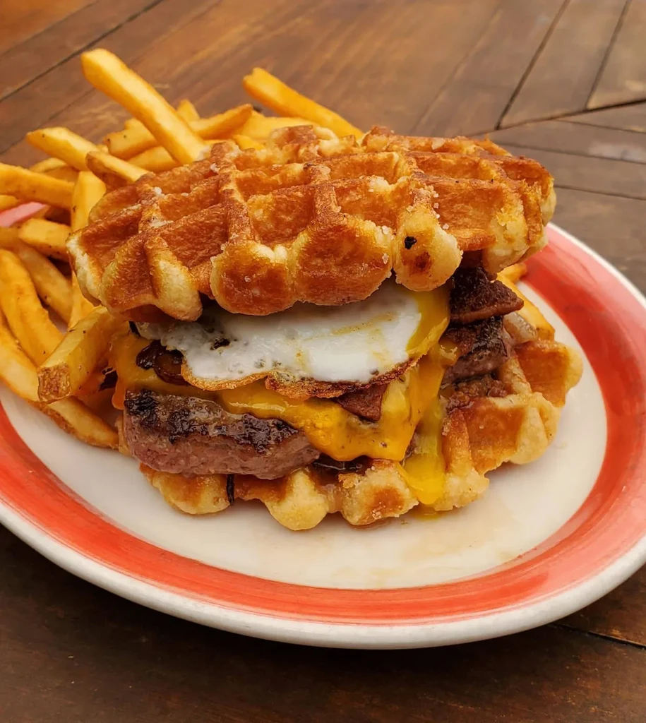 Waffle burger with patty, cheese, bacon, egg, and fries.