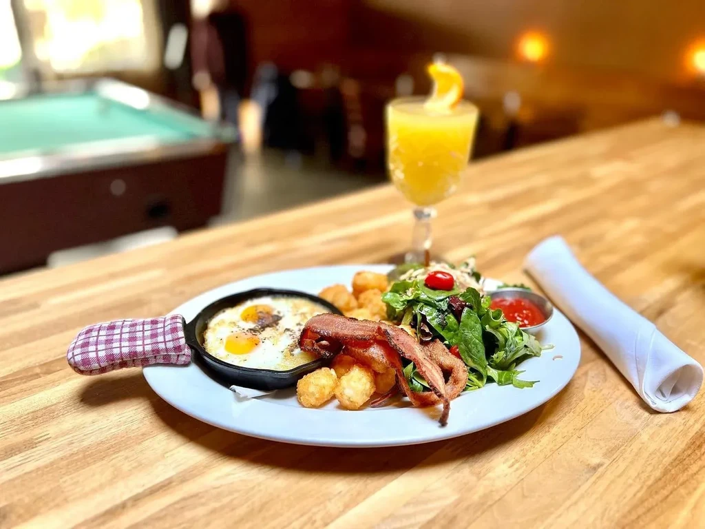 Breakfast plate with sunny-side-up eggs, bacon, tater tots, salad, orange drink.