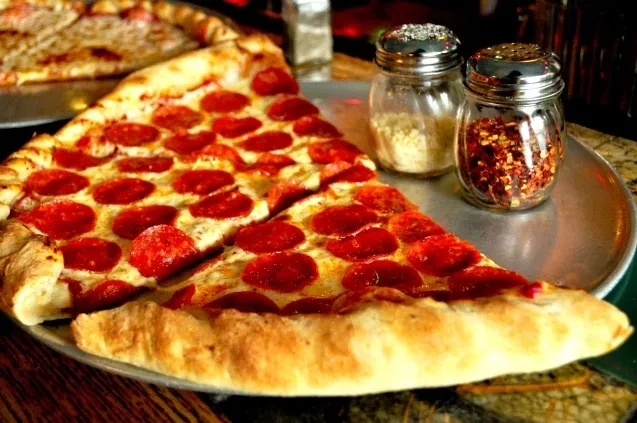 Close-up of pepperoni pizza slices with grated cheese and pepper flakes.