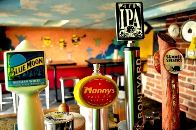 Sharp image of beer tap handles against a blurred, vibrant bar mural.