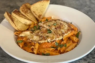 Penne pasta with grilled chicken, creamy red sauce, and garlic bread.