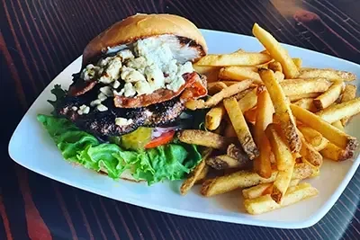 Gourmet burger with blue cheese, bacon, nuts, and seasoned fries.