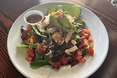 Well-plated chicken and avocado salad with bacon, tomato, and dressing.