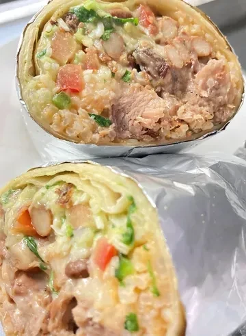 Large burrito half, cut open, revealing meat, rice, beans, and vegetables.