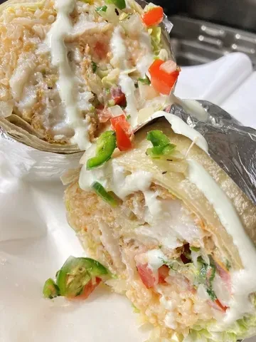 Halved burrito showing rice, protein, vegetables, jalapeños, and creamy sauce.