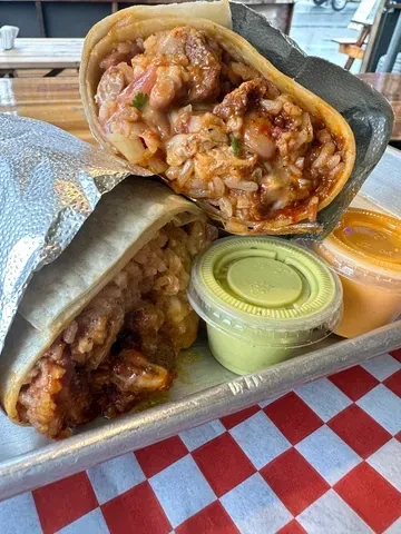 Two burritos, one cut revealing meat, rice, beans, and sauces.
