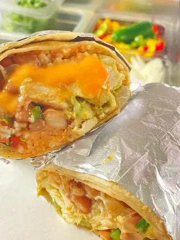 Half-cut burrito showing rice, beans, greens, and cheese, in a kitchen setting.