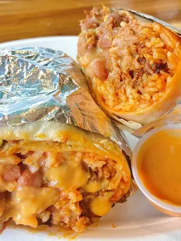 Halved burrito with rice, beans, meat, cheese, and orange dipping sauce.