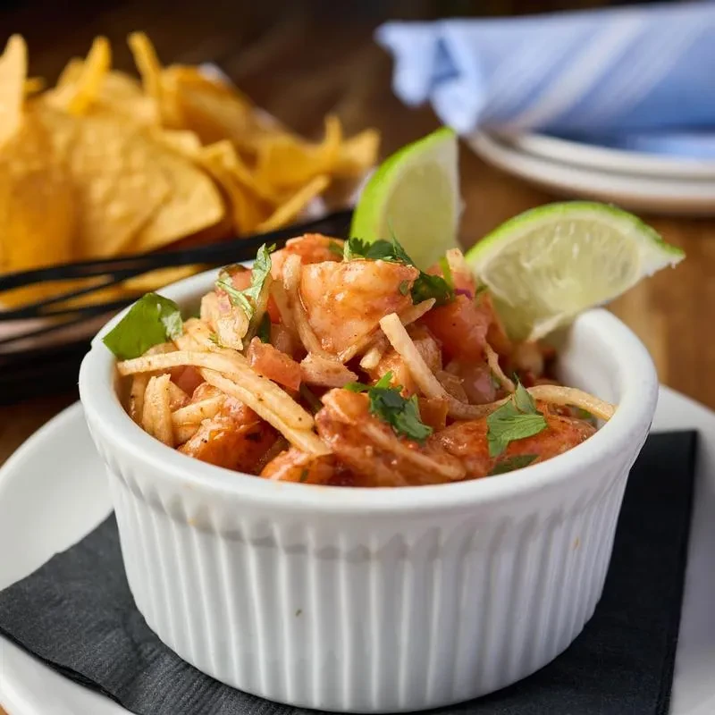 Shrimp ceviche with tomatoes, cilantro, and lime in a white ramekin.