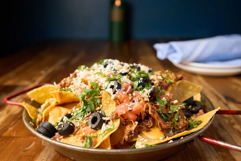 Loaded nachos in a metal pan with meat, cheese, tomatoes, and olives.