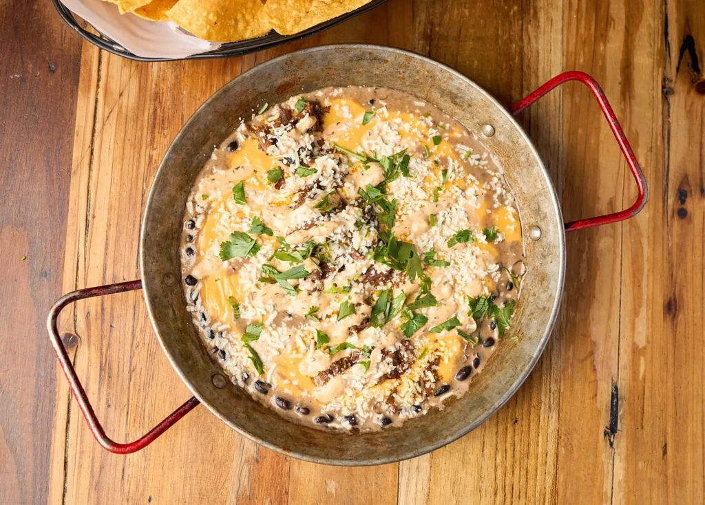 Pan of creamy bean dip topped with cheese, shredded meat, cilantro.