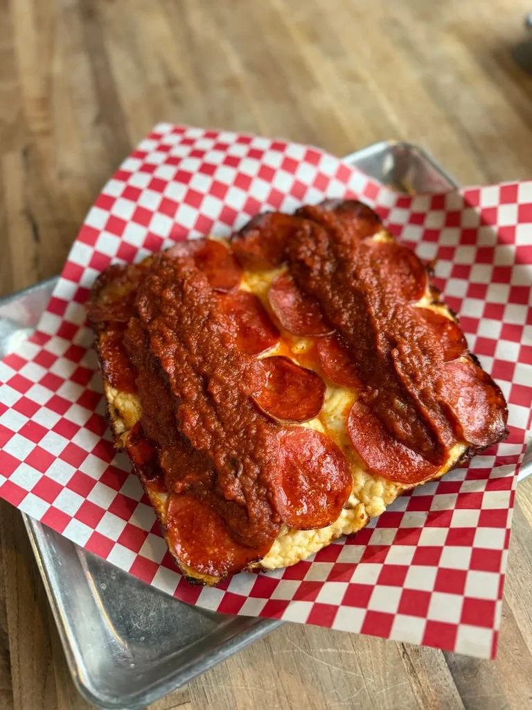 Square pizza slice with pepperoni, melted cheese, and drizzled sauce.