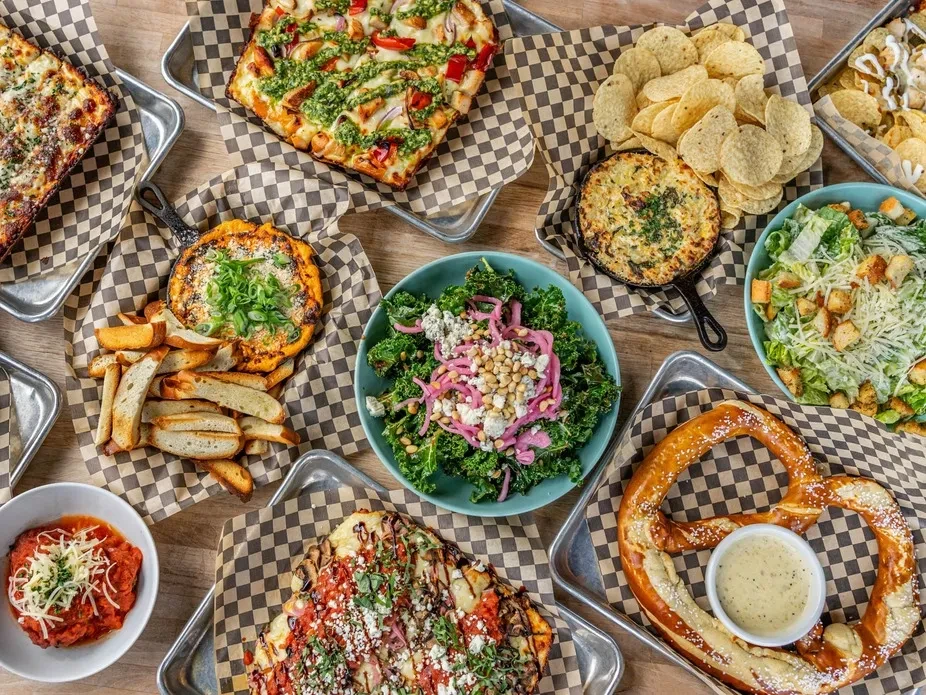 Overhead photo of diverse pizzas, dips, salads, and a soft pretzel.