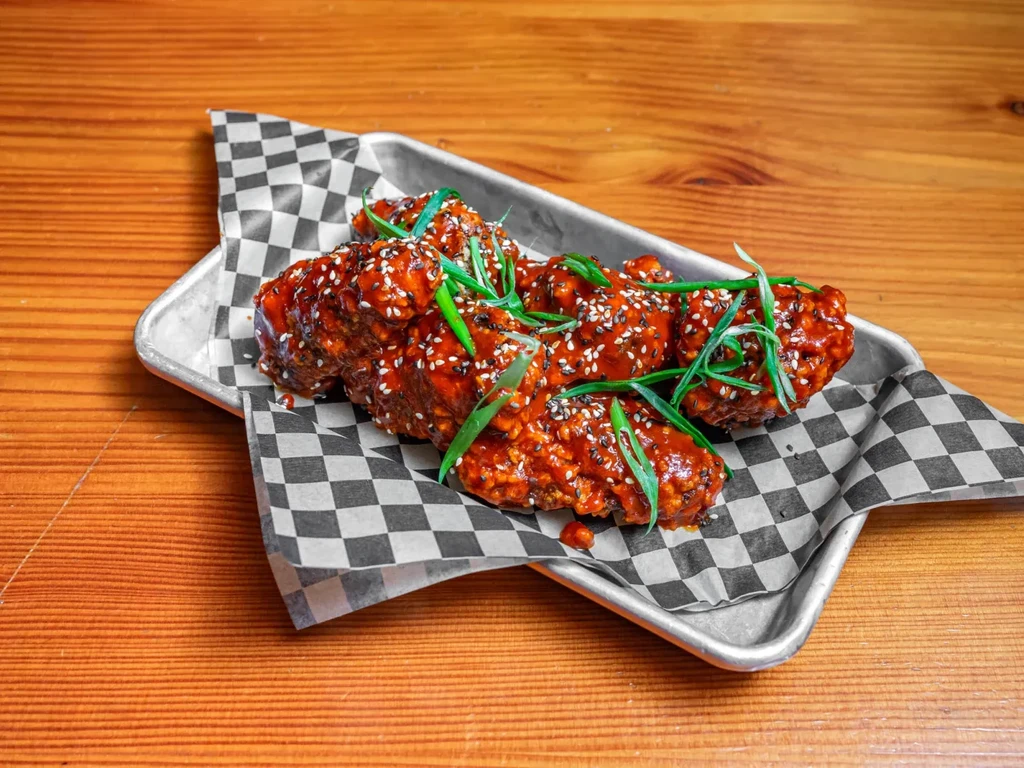 Glazed chicken wings with sesame seeds and scallions on a metal tray.