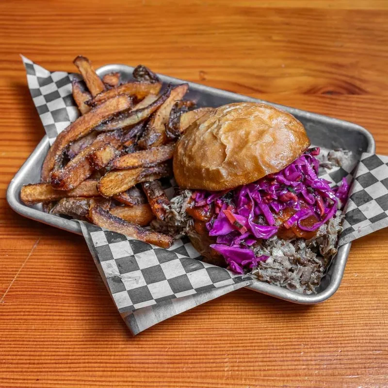Hearty sandwich with purple slaw and fries on a deli-lined tray.