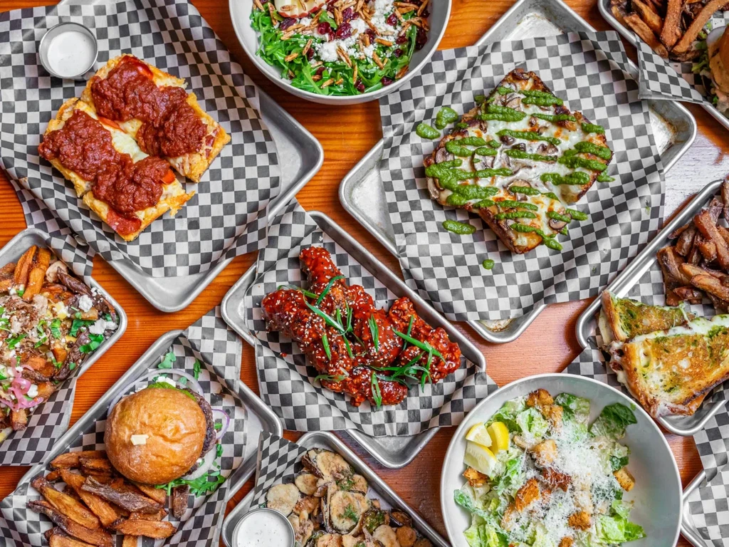 Flat lay of multiple food dishes, including pizza, salads, and wings.
